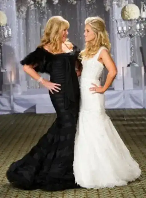 Two women in elegant evening gowns standing and smiling at each other at an event.