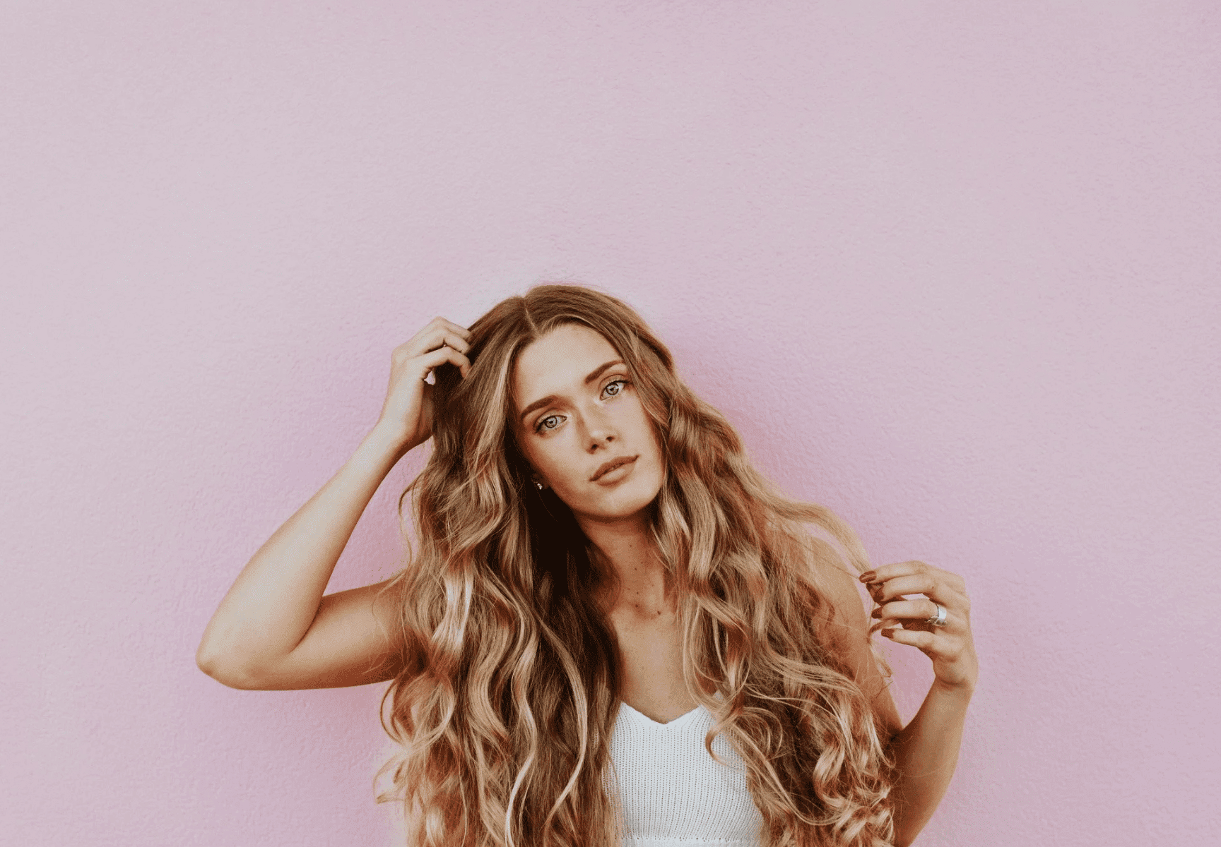 Blonde woman with long wavy hair against a pink background.