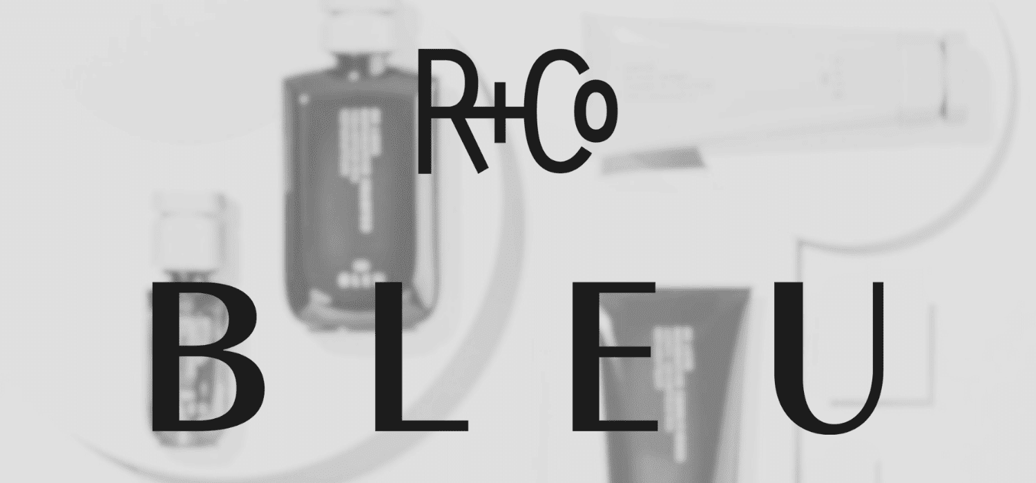 R+Co Bleu haircare products on display with bold branding in the background.