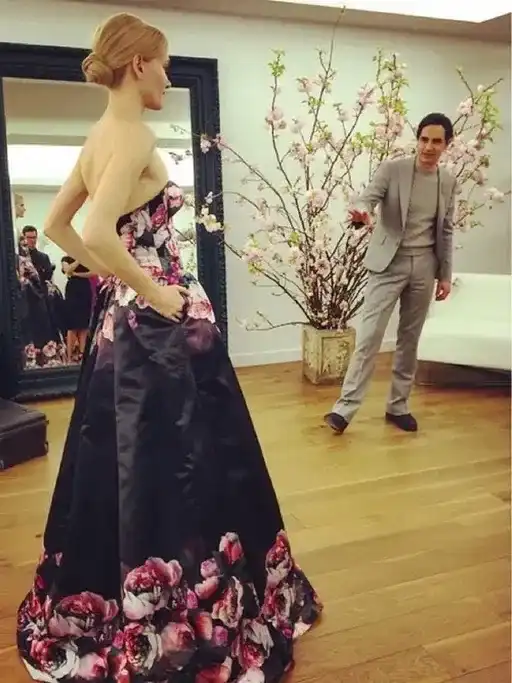 Model in a floral gown with designer in a fitting room with blossoms.